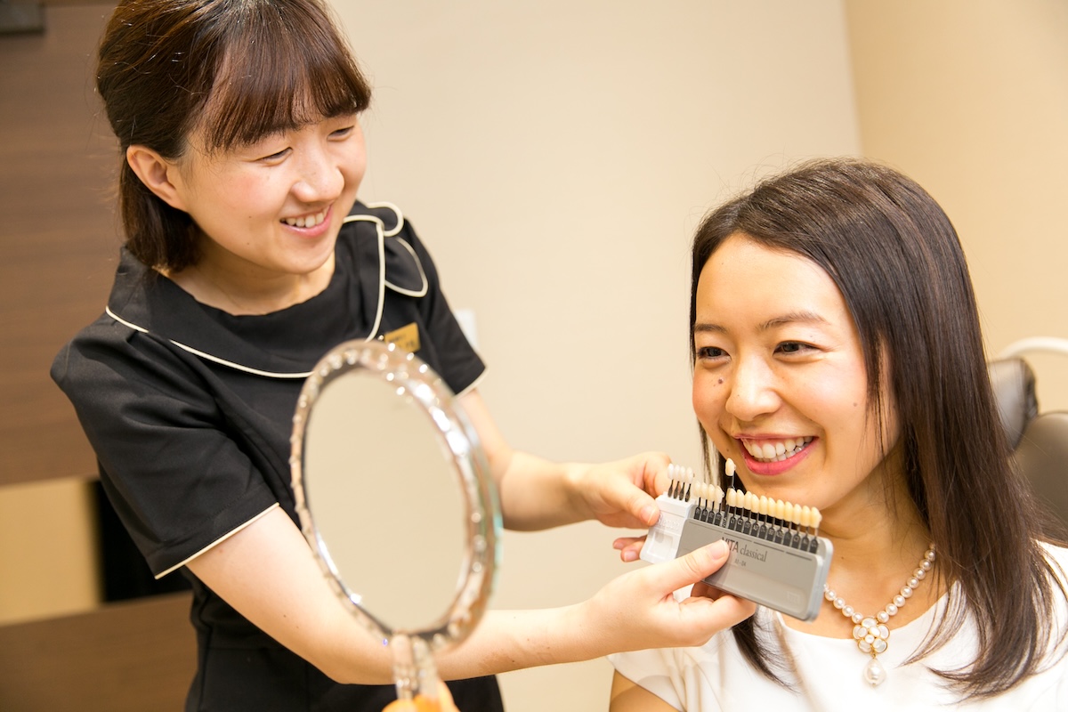 シェードガイドと鏡で歯の色を確認するセラピストと笑顔の患者さん